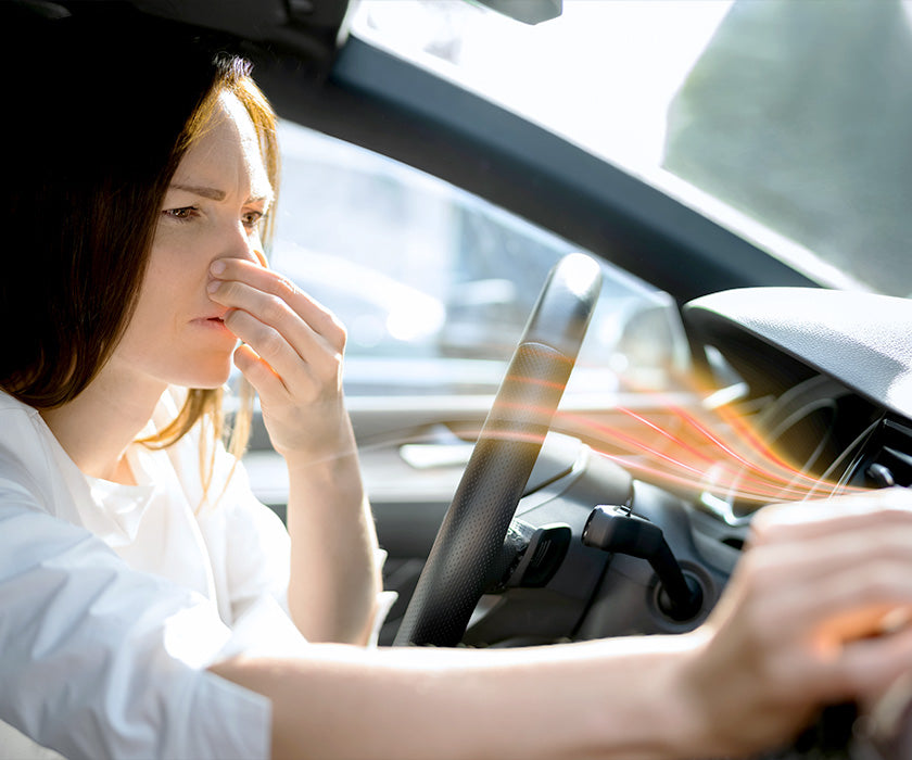 Woman holding nose in car with bad air coming inside of her car